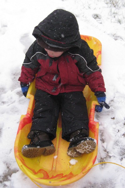 photo of a child sitting in a sled on some snow