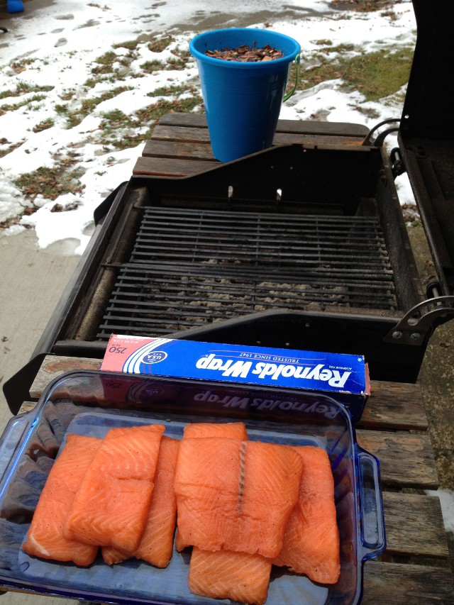 grill with bucket of wood chips and pan of salmon