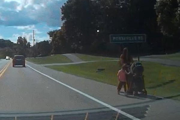 image of mom pushing a stroller and walking with another child on the side of a busy road