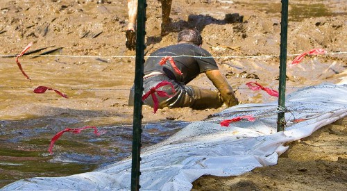 photo of the Muddy Mayhem obstacle in Warrior Dash, showing someone crawling through mud and barbed wire