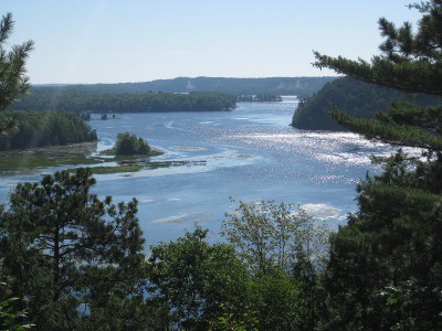 picture of the tree-lined Au Sable river with the sun sparkling on the waves